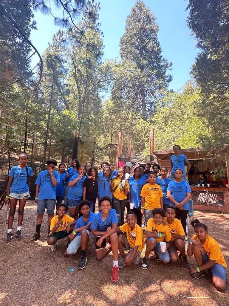 Youth campers in matching blue and yellow shirts posing among tall pines at summer camp