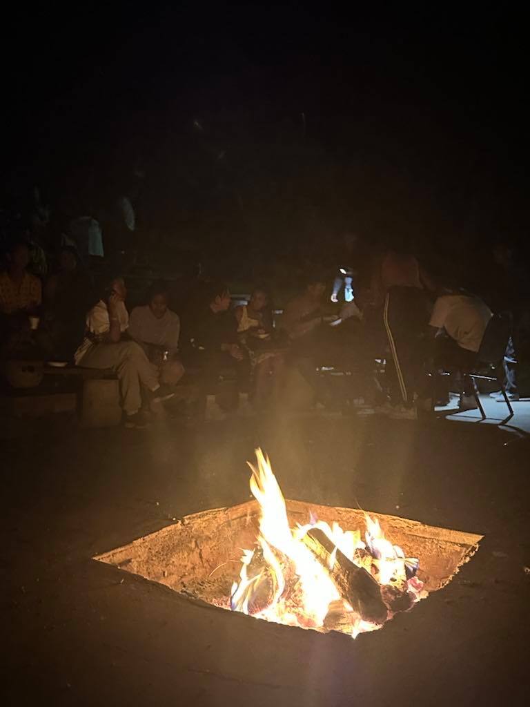 Fellowship members gathered around a glowing campfire pit at night