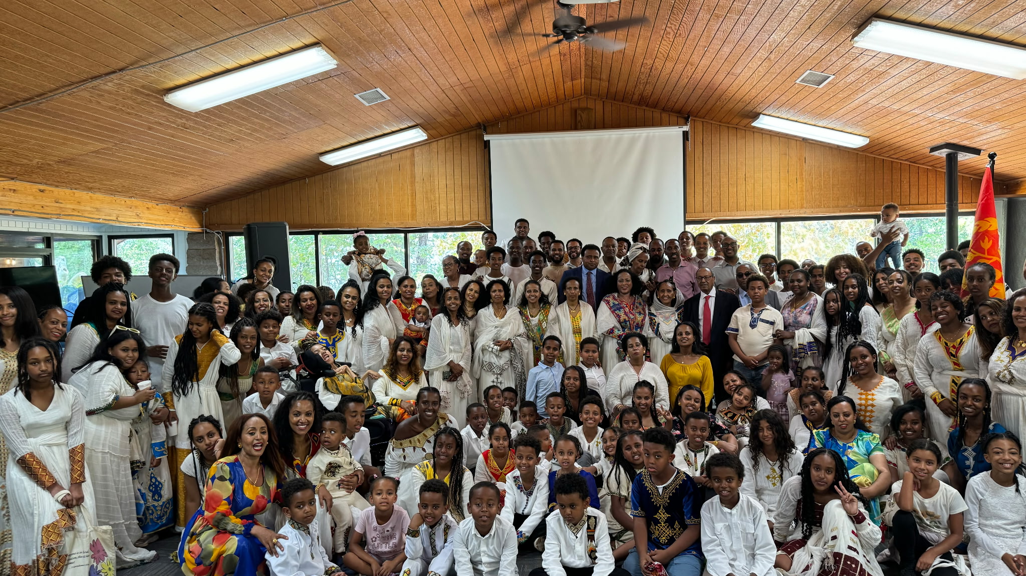 Families in traditional attire posing for a large group photo in a fellowship hall