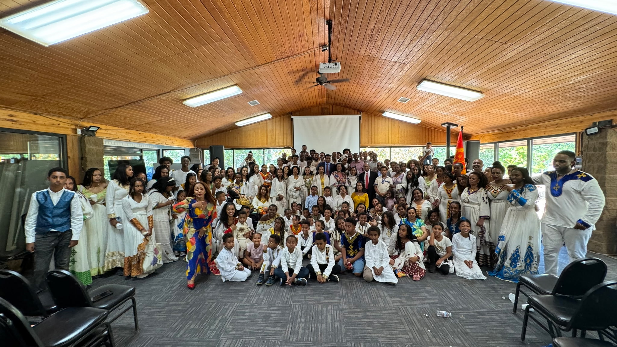 Congregation in traditional white attire gathered for a group photo inside a fellowship hall